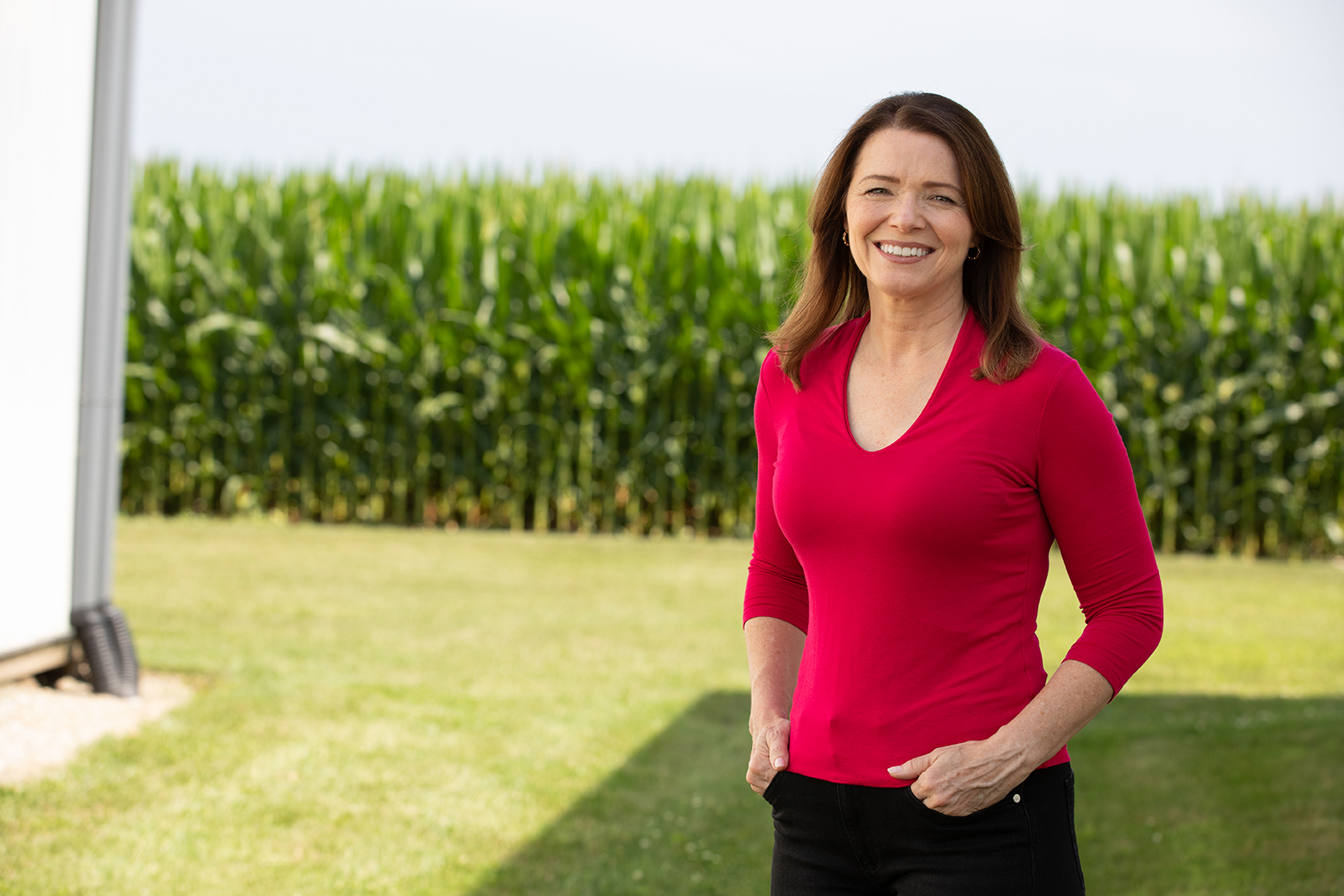 Christina Bohannan in a red top standing and smiling in front of a green cornfield