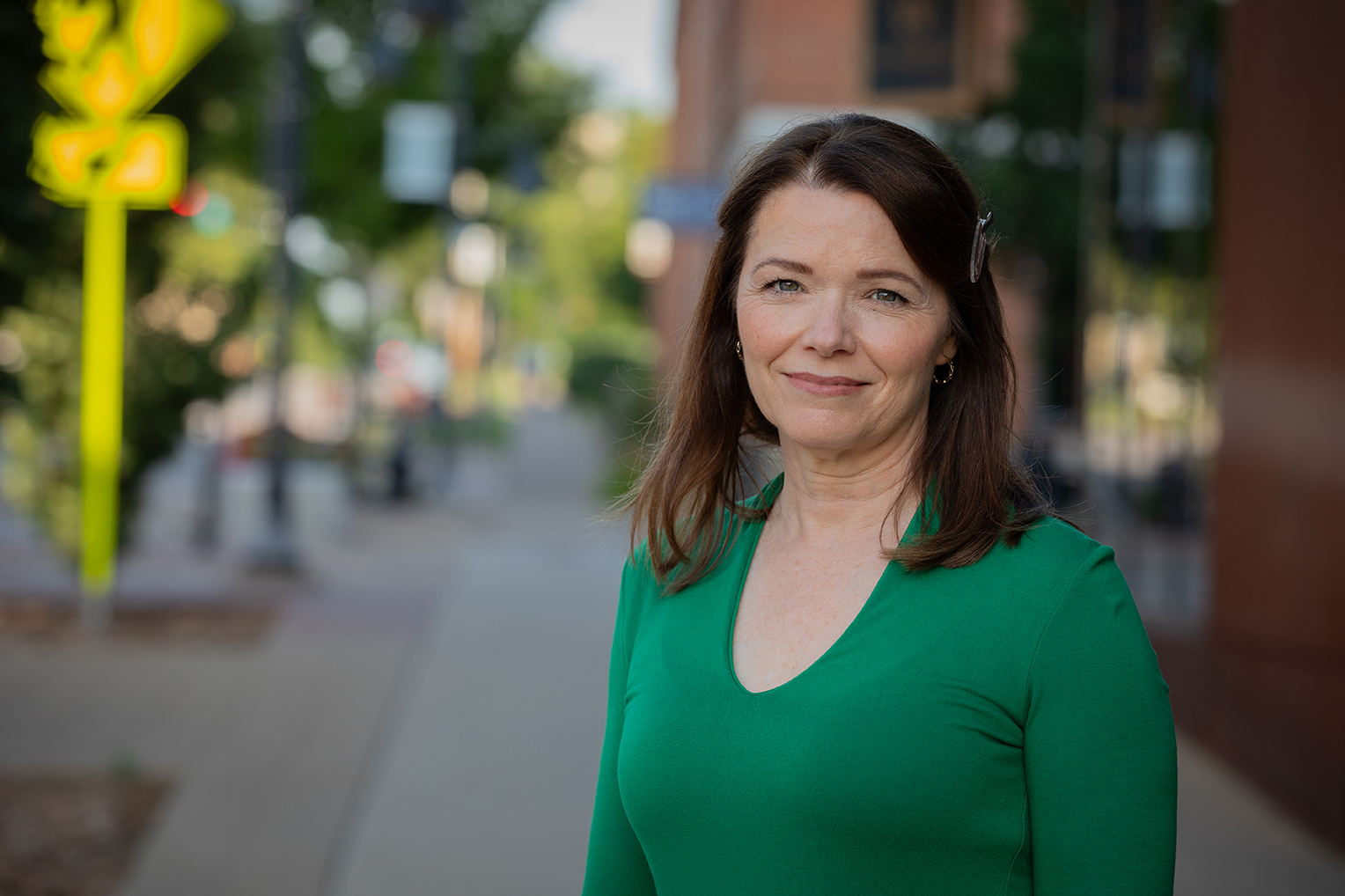 Christina Bohannan in a green top standing on a downtown sidewalk with blurred storefronts behind her