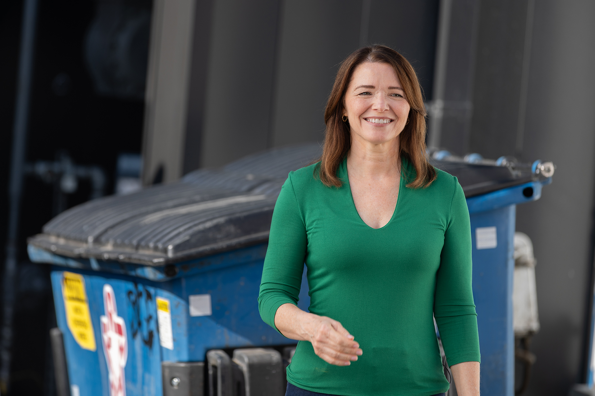 Christina Bohannan in a green top smiling and standing in front of a blue dumpster outdoors
