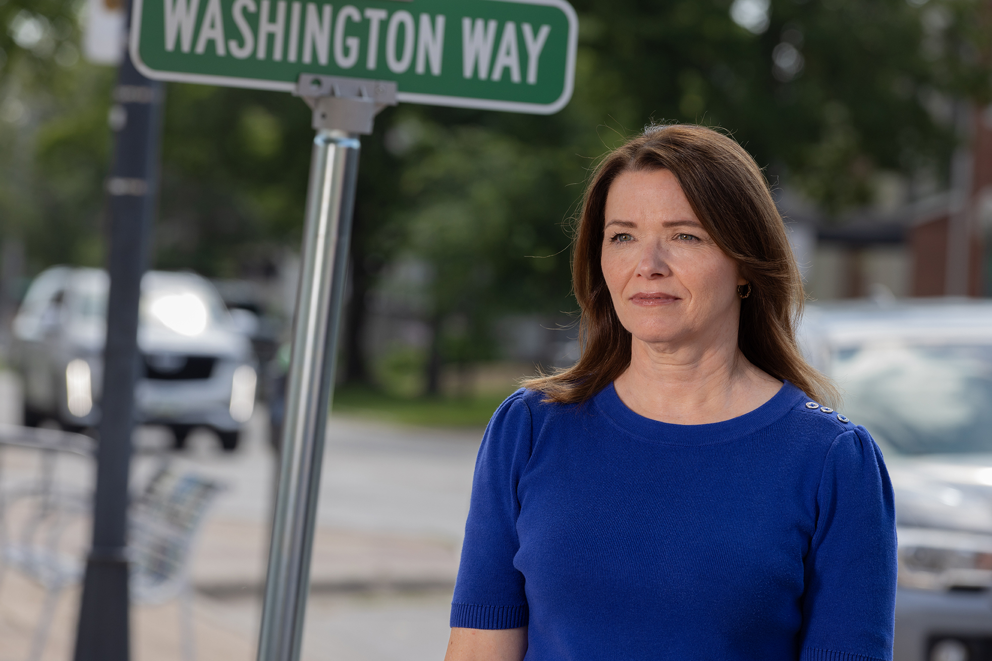 Christina Bohannan in a blue sweater standing on a sidewalk in front of a green Washington Way street sign